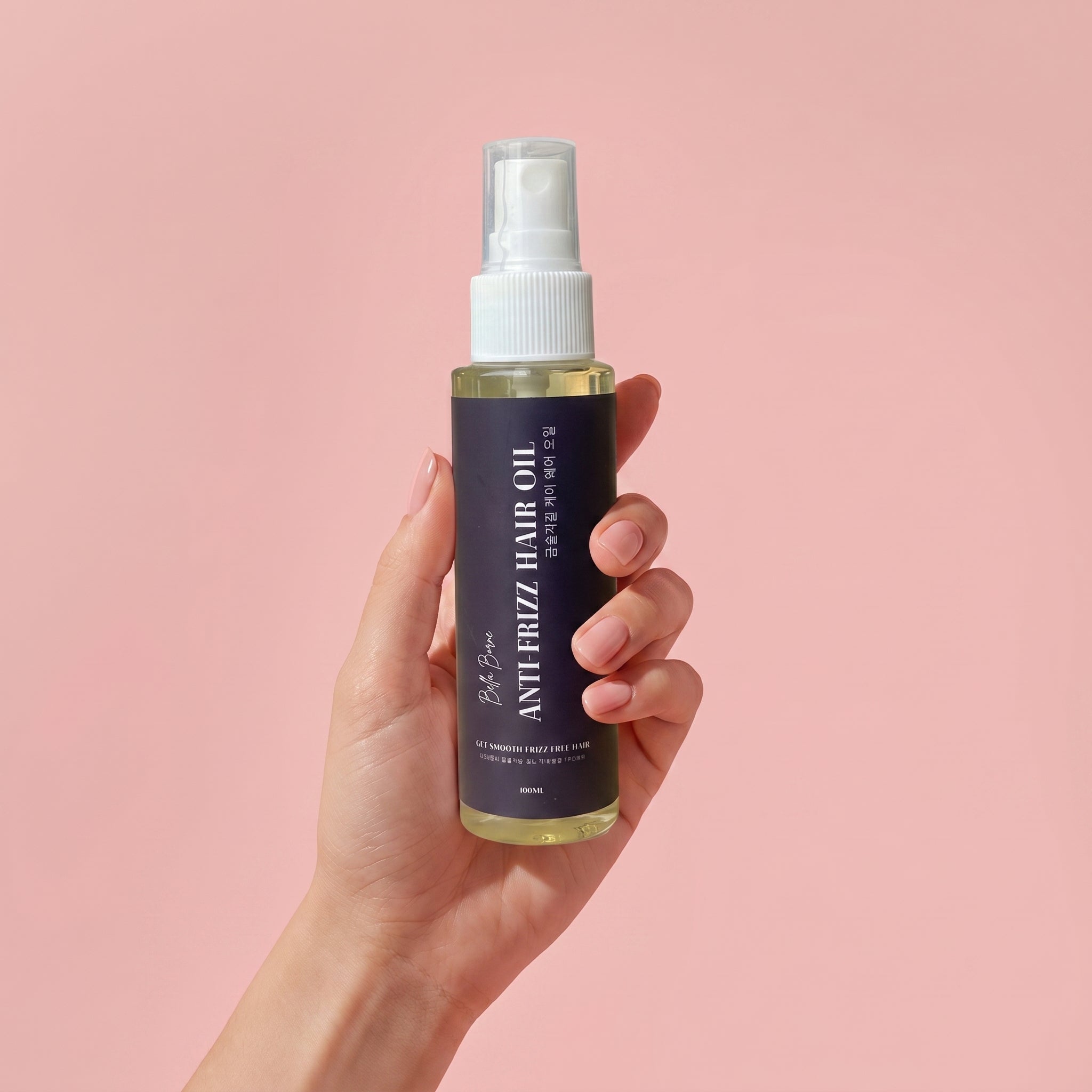 Hand holding a bottle of anti-frizz hair oil against a pink background