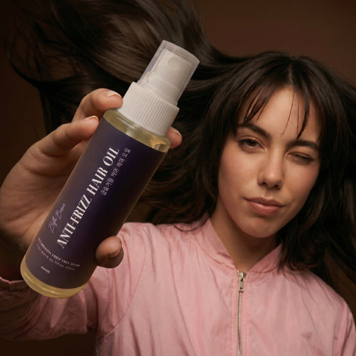 Person holding a bottle of Antifrizz Hair Oil with a brown background