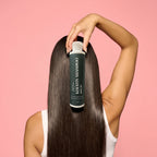 Person holding a bottle of shampoo against long hair on a pink background