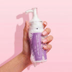 Hand holding a purple bottle of skin-friendly face wash against a pink background