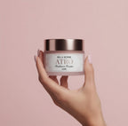 Hand holding a jar of Bella Borne ATRO Radiance Cream against a pink background