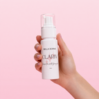 Hand holding a Bella Borne Clariv skincare product against a pink background